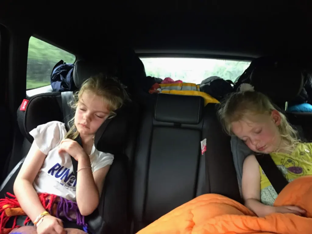 Two kids in the backseat of a moving car, wrapped in blankets, enjoying a long road journey.