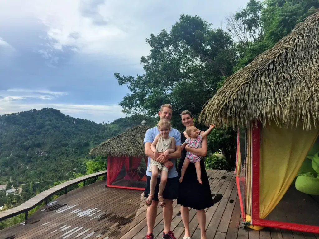 Our family of four standing on a wooden deck at Jungle Club, Koh Samui, enjoying a scenic view of lush green hills and tropical surroundings in Thailand, perfect for a family itinerary with kids.