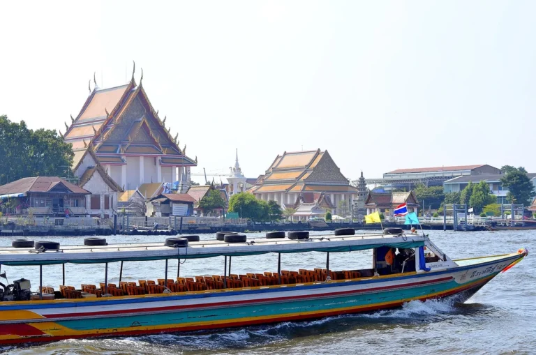 Long-tail boat on the Chao Phraya River in Bangkok, Thailand, with traditional Thai temples in the background, showcasing vibrant river life and cultural heritage.