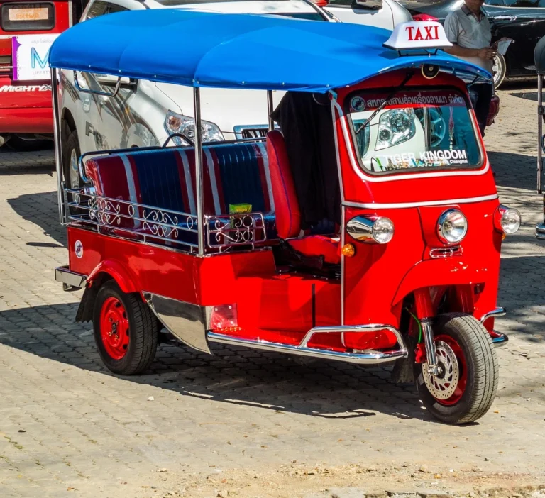 Brightly colored tuk-tuk taxi in Bangkok, Thailand, featuring red and blue accents and striped seats, parked on a paved area.