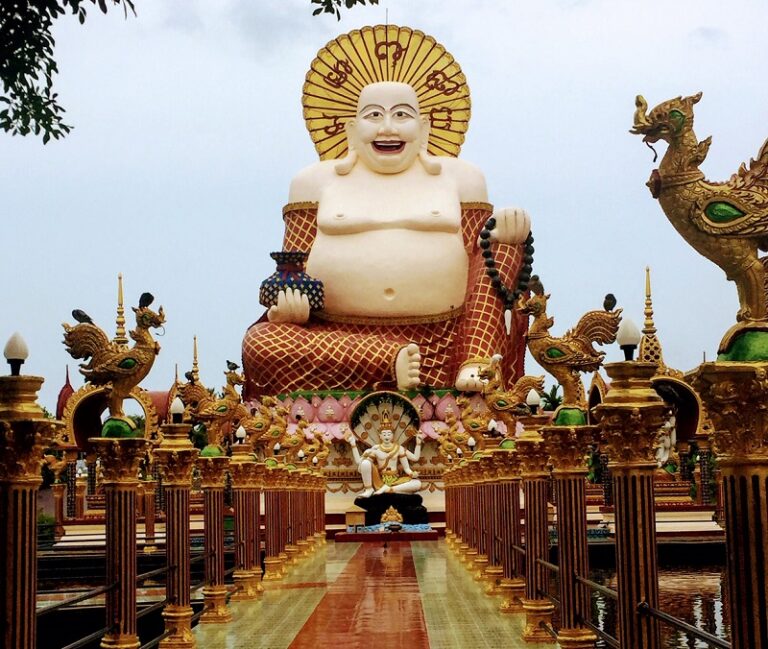 Buddha statue at Wat Plai Laem in Bophut, Koh Samui, Thailand, surrounded by ornate golden decorations and dragon-like figures.