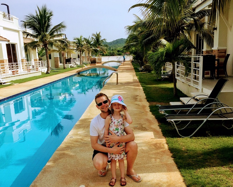 Swimming pool at Oriental Beach Pearl Resort in Sam Roi Yot, Thailand, flanked by palm trees and resort buildings, with a scenic mountain view.
