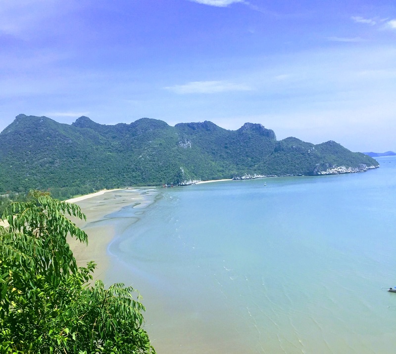 Scenic view of Thailand's coastline with green mountains, a sandy beach, and clear blue sea, captured during the climb to Phraya Nakhon Cave.