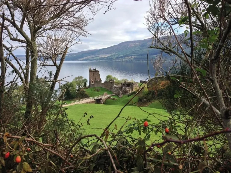 Urquart Castle in Inverness the distance through the trees with Loch Ness behind it.