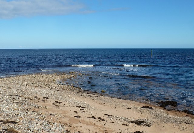 Golden sandy beach at Brora, Scotland, with gentle waves and grassy dunes under a partly cloudy sky.