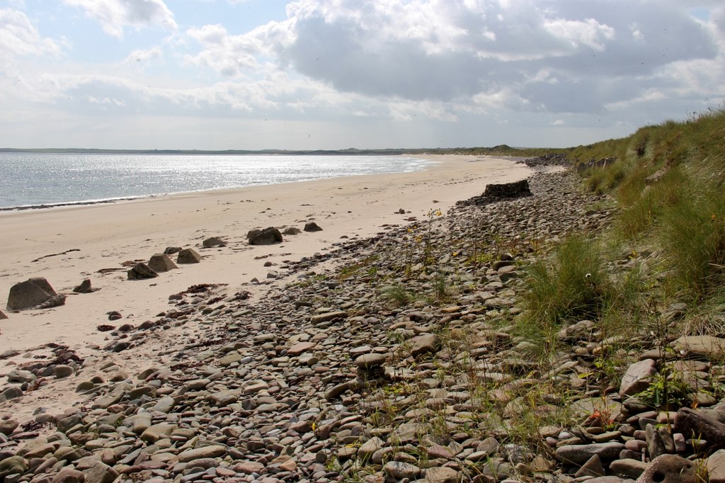 Scenic view of Keiss Beach, Caithness, with rocky coastline and clear blue waters under a bright sky.