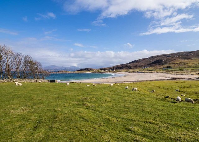 Golden sands of Mellon Udrigle beach with calm waters, distant hills, and a soft, clear sky.