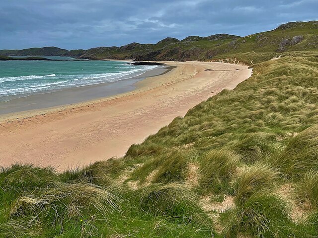 Wide view of Oldshoremore Beach with golden sand, turquoise water, and surrounding grassy hills.