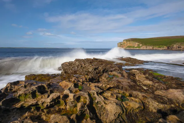Rugged rocky shoreline of Peedie Sands Beach in Caithness, Scotland, with large boulders and the North Sea under a partly cloudy sky.