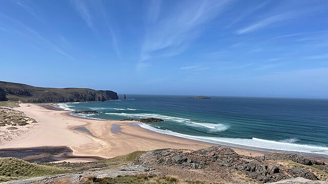 Wide sandy beach at Sandwood Bay, with cliffs and distant sea stack under a bright, clear sky.
