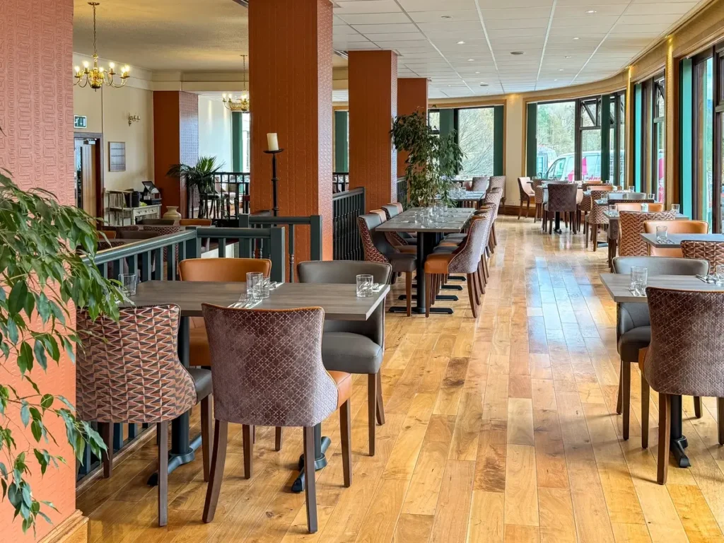 A warm and inviting hotel bar in Ullapool, Scotland, featuring wooden furnishings, a long counter with barstools, and an array of spirits displayed on shelves. The space is softly lit, creating a relaxed atmosphere.