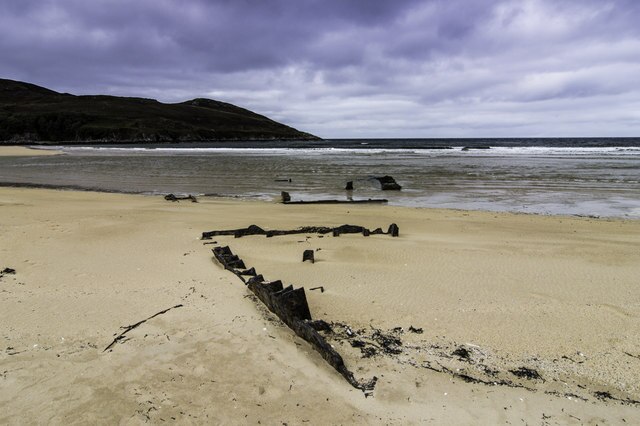Rusted remains of the SS John Randolph shipwreck on the shore, partially submerged in water, with coastal rocks in the background.