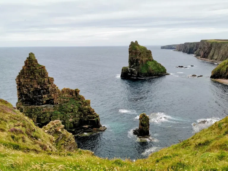 Duncansby Stacks, two towering sea stacks off the coast of Scotland, surrounded by rugged cliffs and ocean waves.