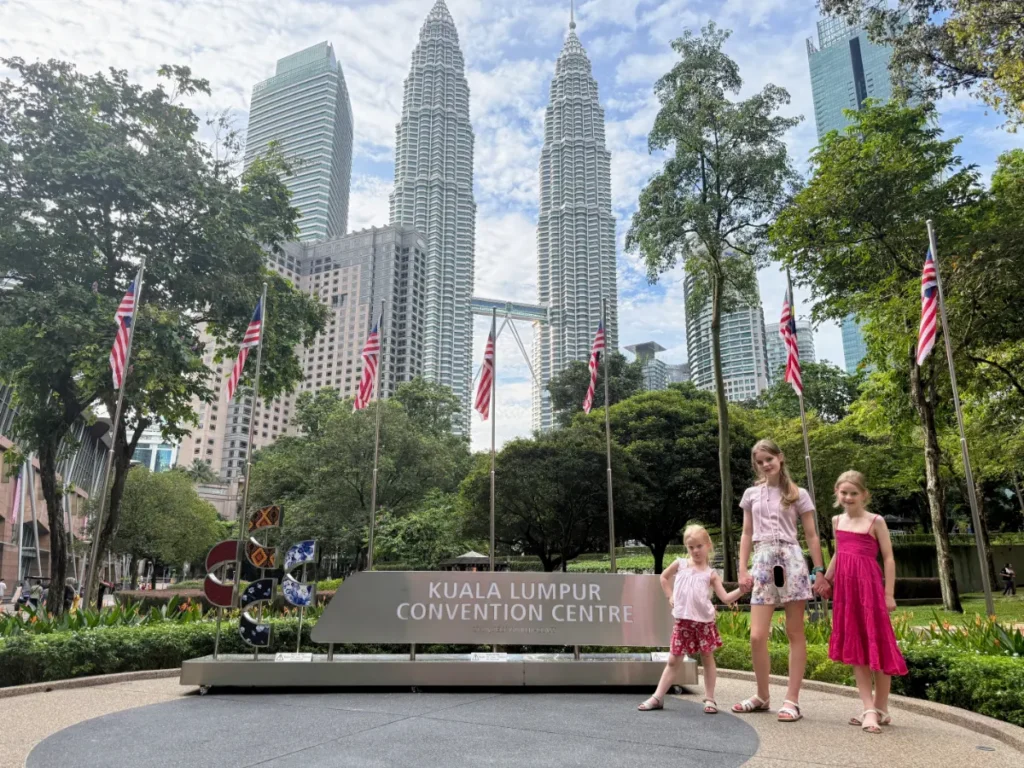 Our children posing in front of Kuala Lumpur Convention Centre with Petronas Towers in the background—getting around Malaysia as a family