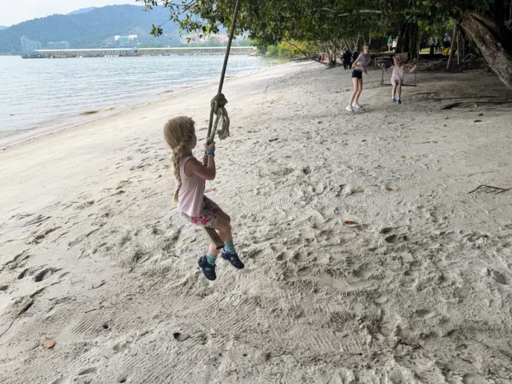 Our youngest child swinging on a rope at Penang National Park beach—playful family moment surrounded by nature during our Malaysia itinerary
