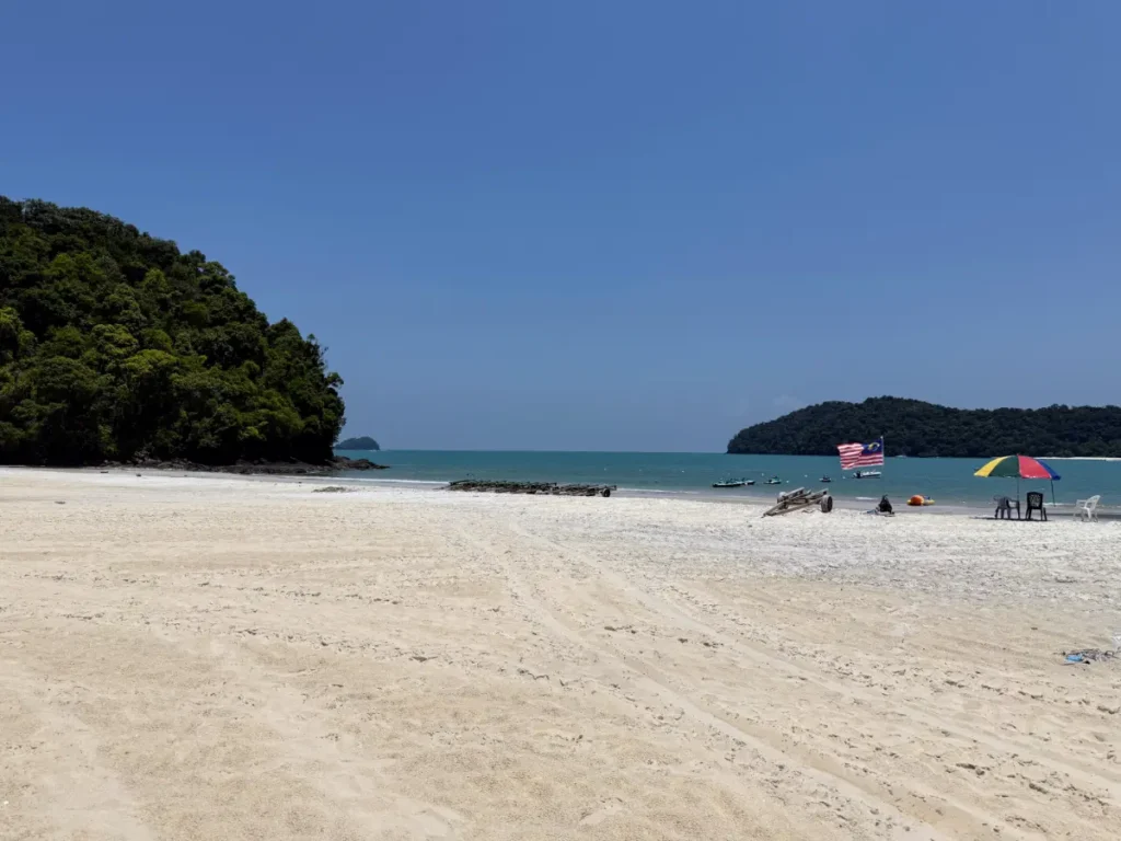 Pantai Tengah beach in Langkawi with turquoise waters, Malaysian flag, and colourful umbrella
