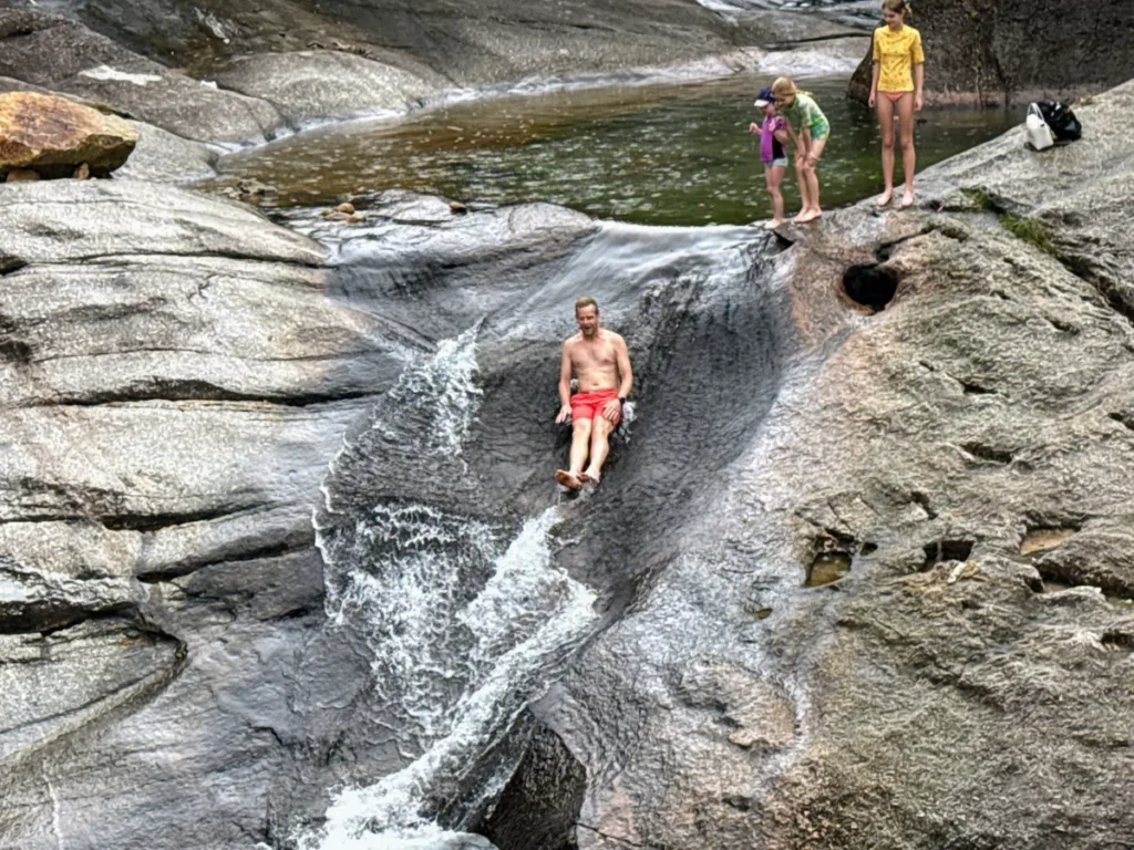 Dad sliding down Seven Wells Waterfall in Langkawi—natural waterslide and adventure highlight on our Malaysia itinerary.