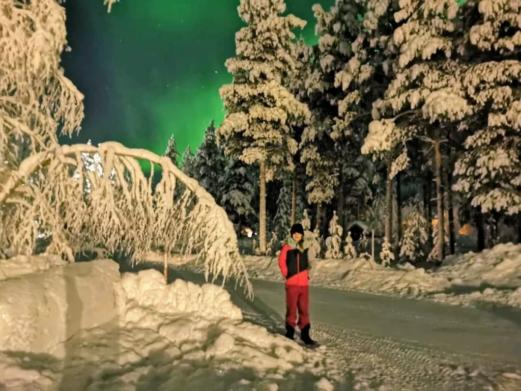 Our daughter in winter gear under Northern Lights in snowy Levi forest