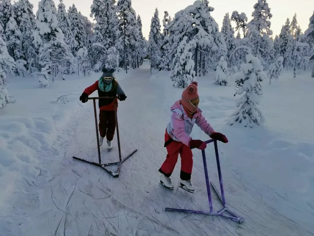 Kids ice skating through a snowy forest trail at Kotatieva Winter Park in Finland.