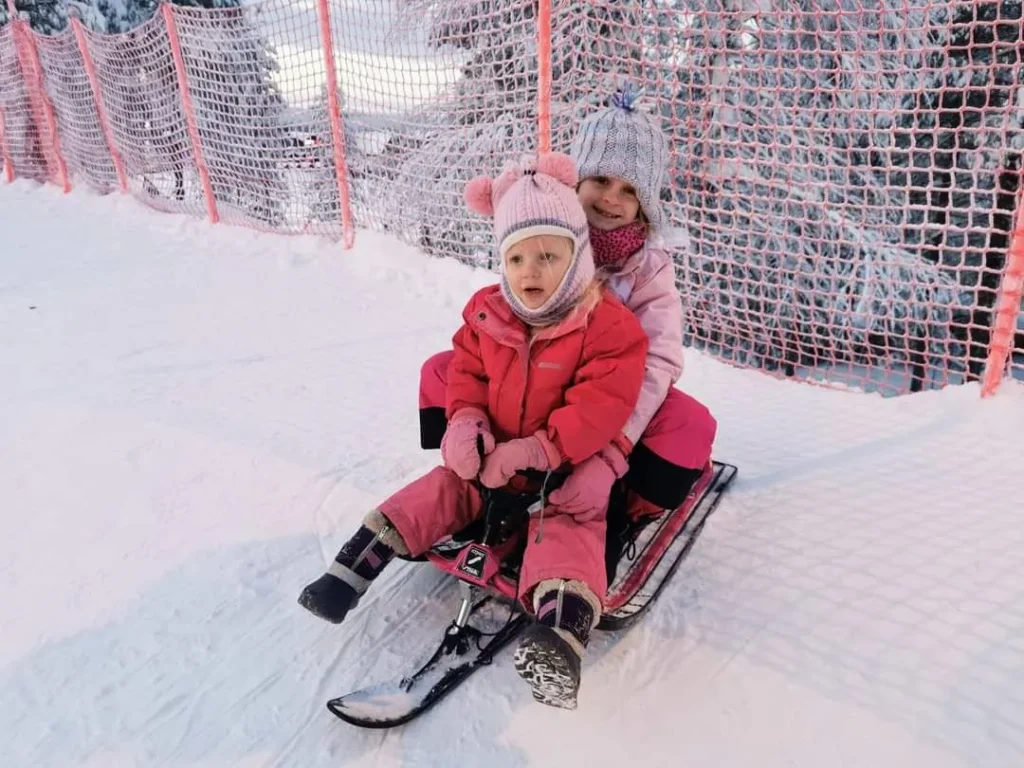 Our two kids sitting on a sled at Kids' Land in Levi, Finland, dressed in colourful snowsuits and ready for snowy fun.