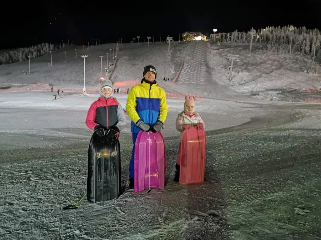 Sledging at night on a snowy slope at Zero Point in Levi, Finland, part of a DIY Lapland itinerary with kids.