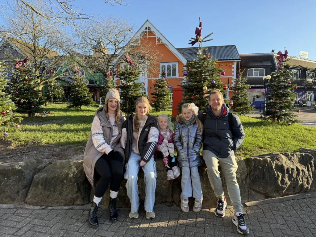 Family sitting in front of decorated Christmas trees and festive buildings at Alton Towers Santa Sleepover