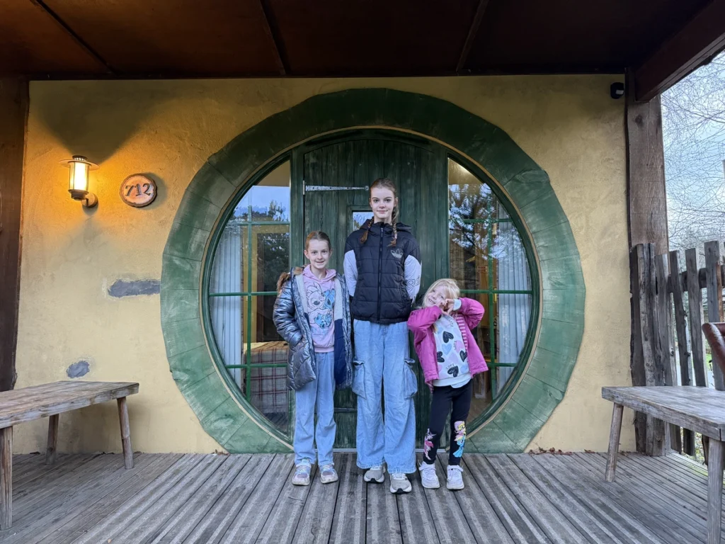 Children standing outside round green Hobbit-style door at Alton Towers Enchanted Village during Santa Sleepover