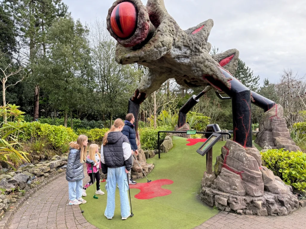 Family playing mini-golf under giant insect sculpture at Alton Towers Extraordinary Golf during Santa Sleepover